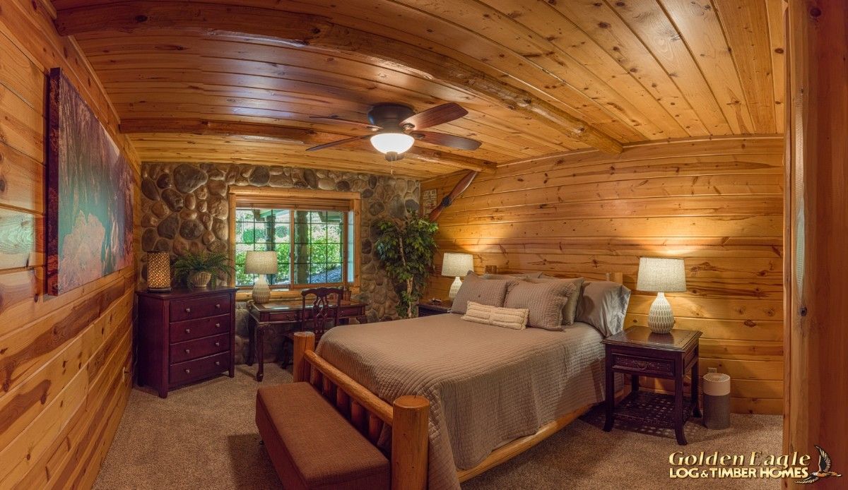 grey bedding on bed against log cabin wall with french doors in background