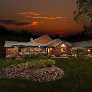 log cabin behind landscaping with sunset in background above home