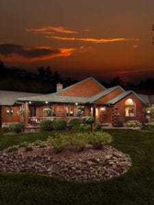 log cabin behind landscaping with sunset in background above home
