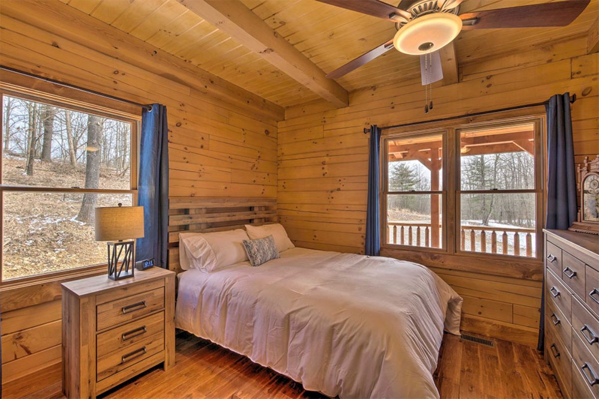 white bedding on bed beside windows and dresser in log cabin