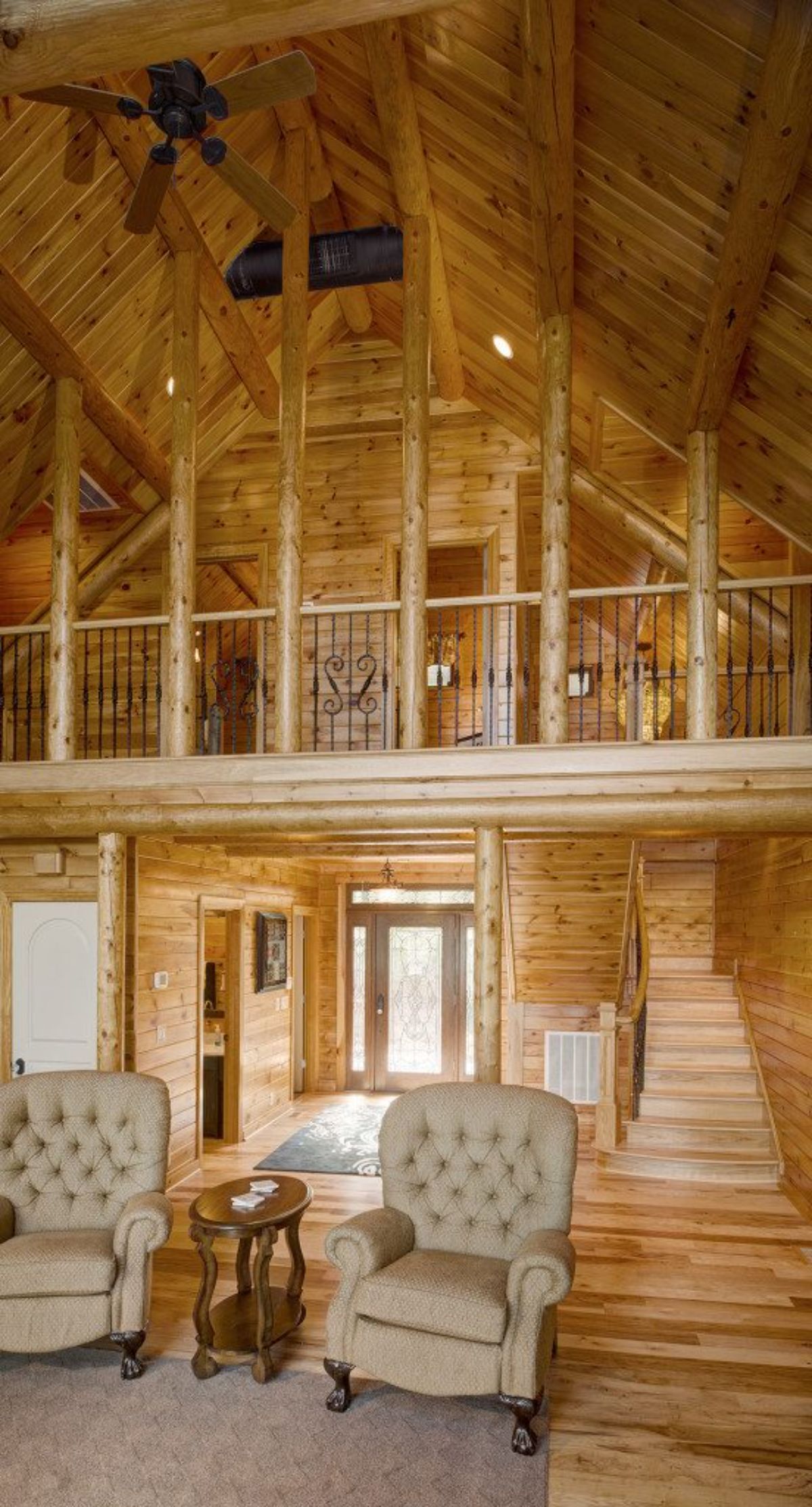 light wood interior of log cabin with cream chairs in foreground and loft in upper background