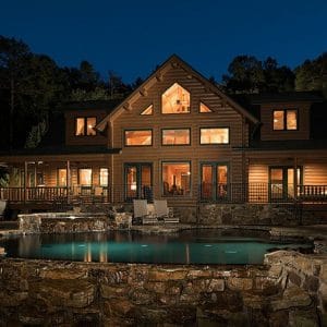 back of log cabin lit after dark with pool in foreground