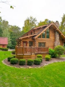 side of log cabin with short shtrubs around outside deck with wood railing