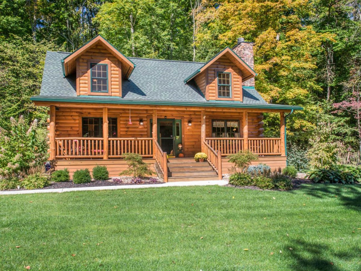 log cabin with green roof two dormer windows and light wood logs on porch