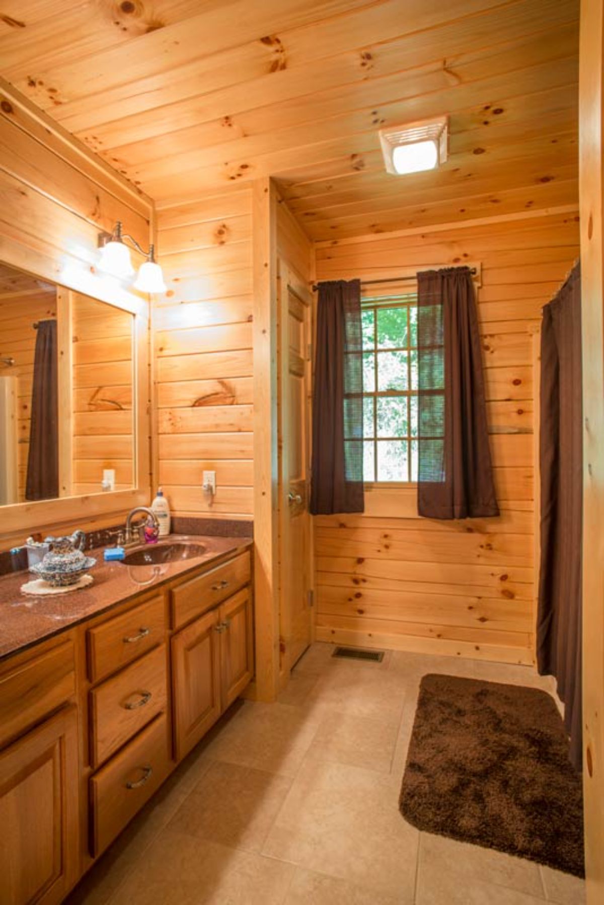 wood vanity with brown curtains on windows in log cabin bathroom