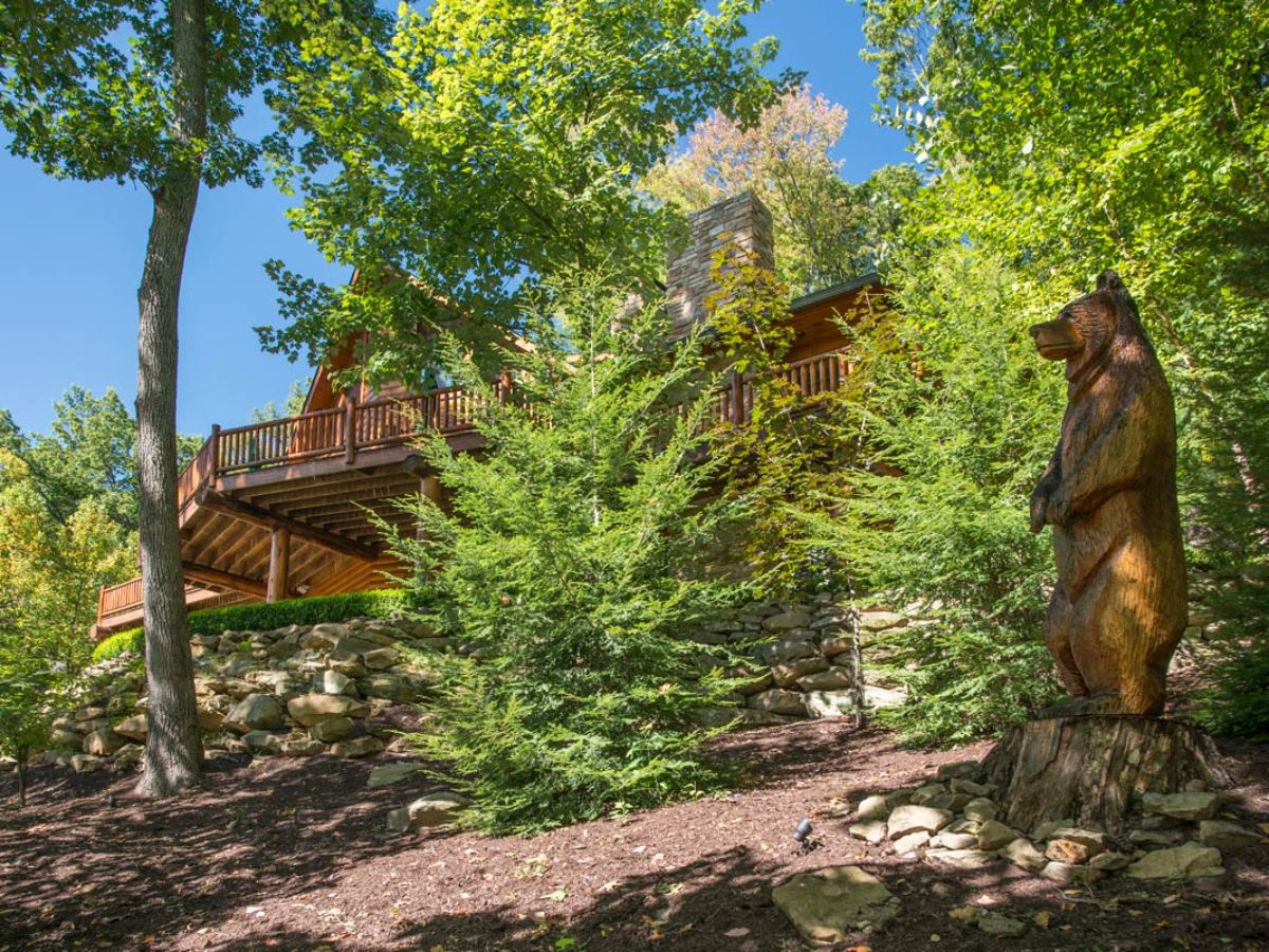 wood bear in front of trees with log cabin in background