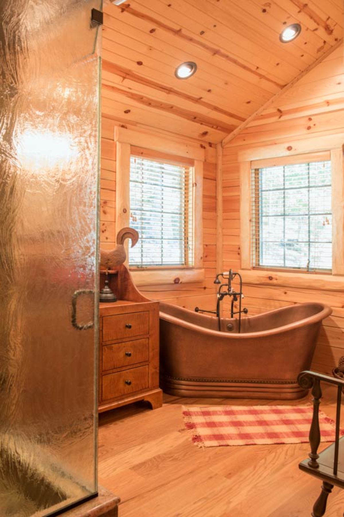 copper soaking tub beneath windows in corner of bathroom with glass shower door in foreground