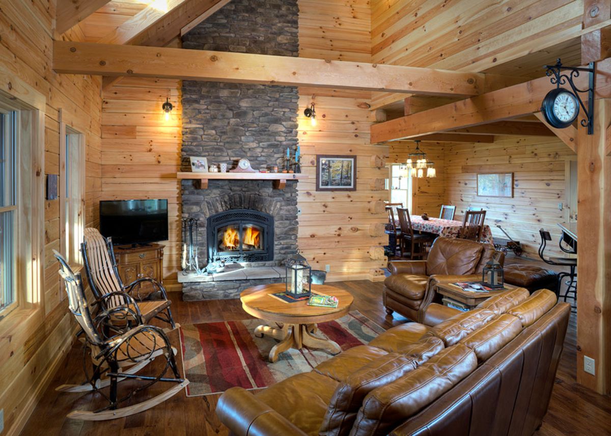 stone fireplace in front of brown leather sofa in log cabin great room