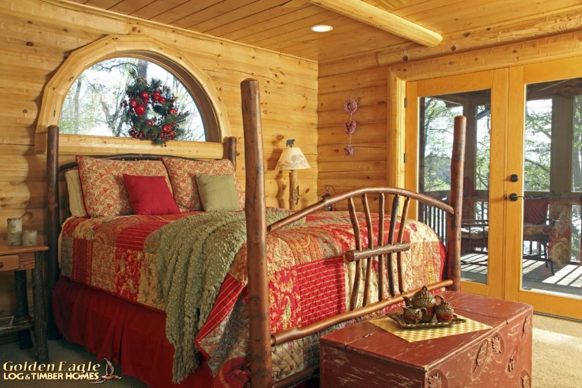 red bedding on wood four poster bed in log cabin with glass doors on right wall