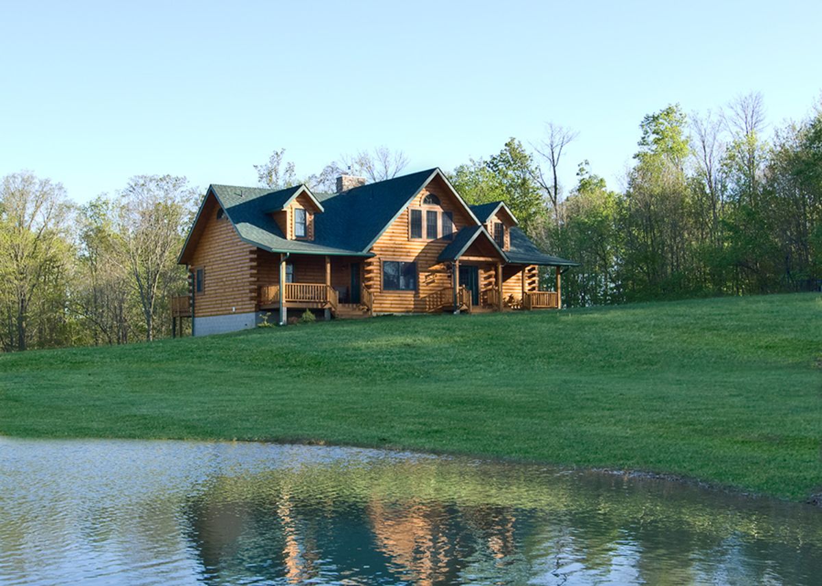 log cabin with green roof behind pond