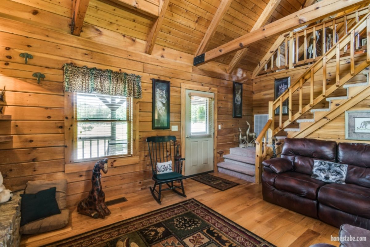 log stairs to loft behind dark brown leather sofa in log cabin