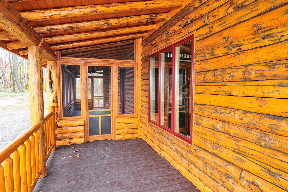 stained wall of log cabin porch with screened window by door at end