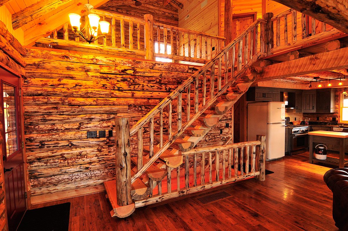 stairs to second floor of log cabin with dark wood stain and kitchen in background