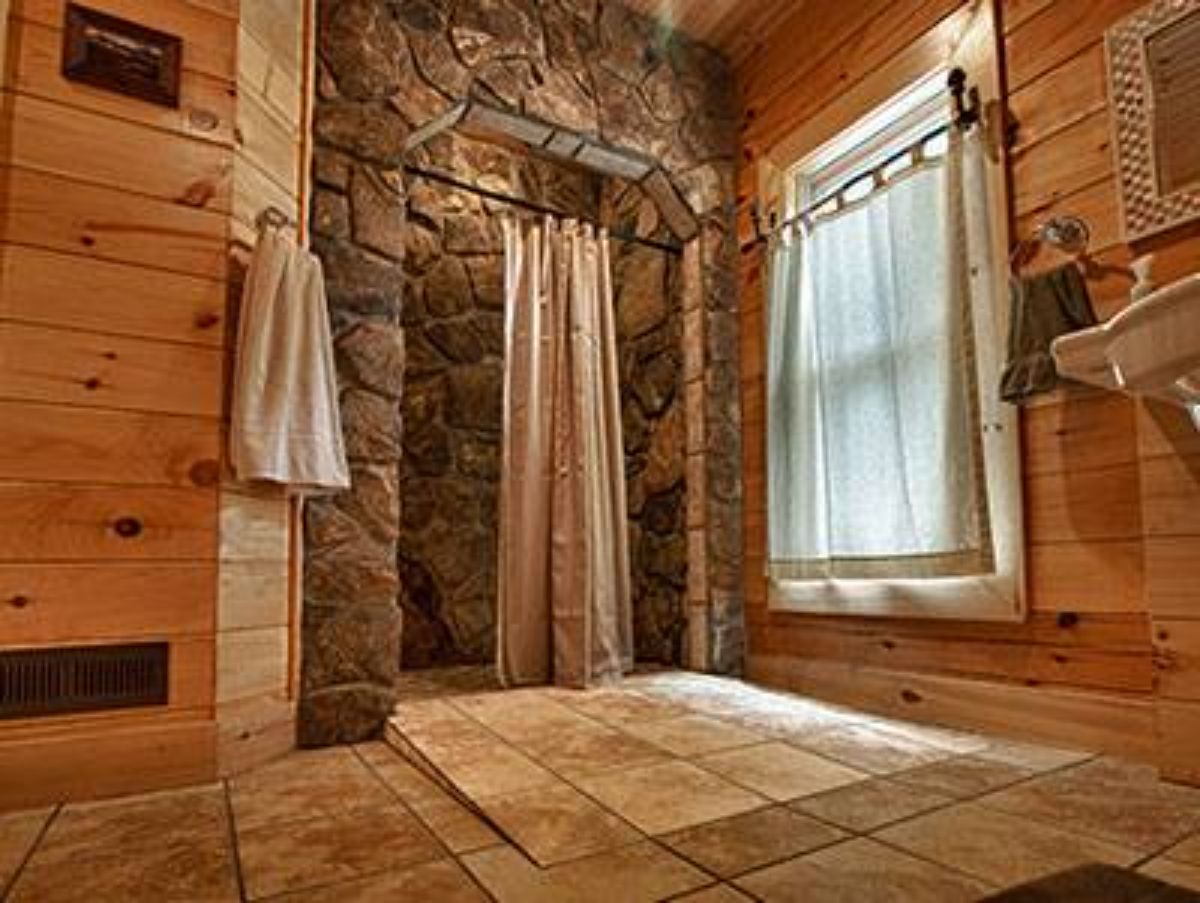 stne shower in master bathroom with white rug under window