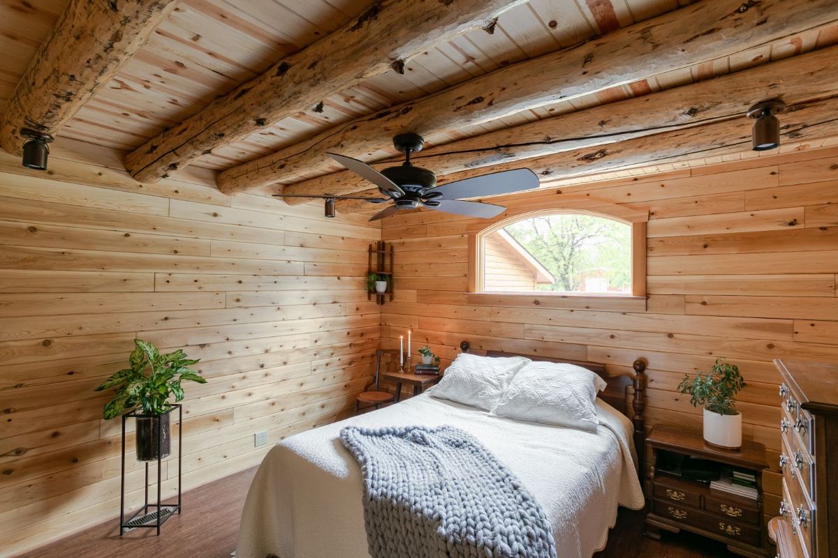 white linens on bed in log cabin with small window above