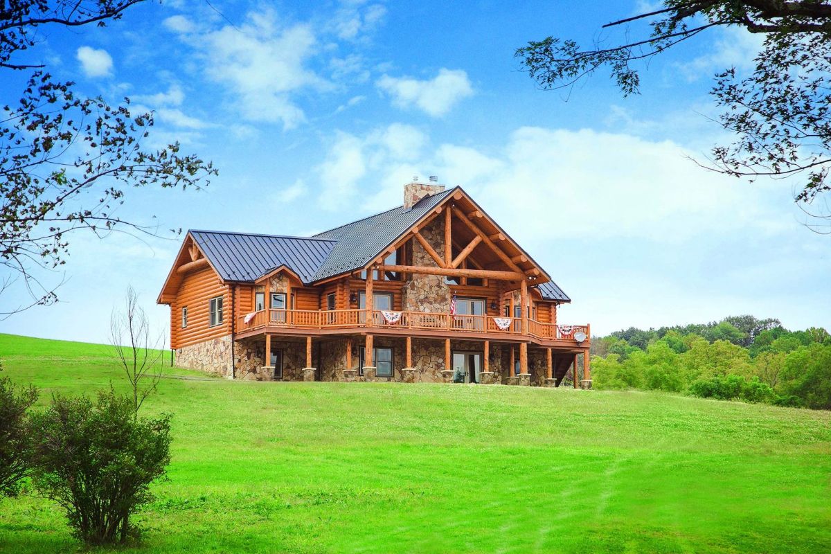 log cabin with decks on back sitting on green hill