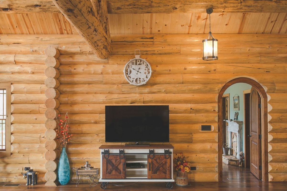 tv against log cabin wall with arched open doorway on right of image