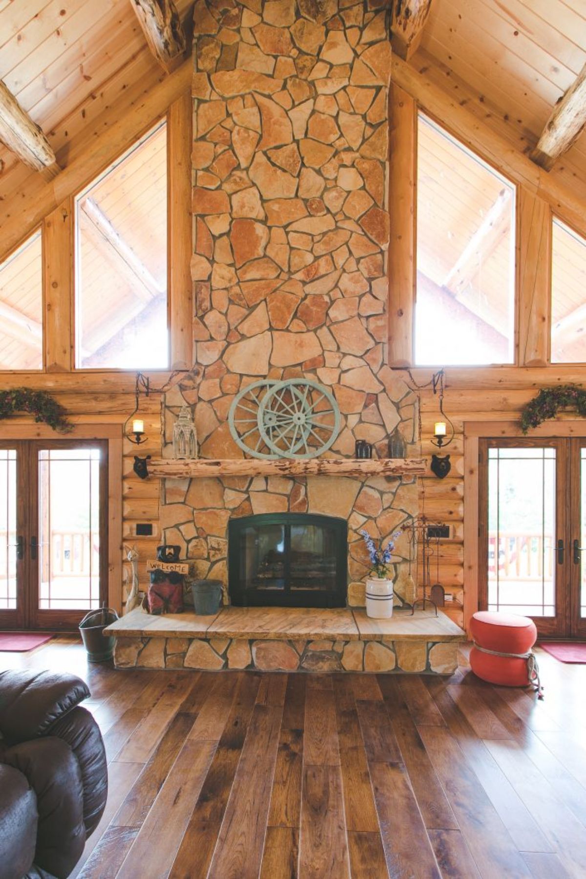 stone fireplace with windows and doors on both sides and wagon wheel decor on mantle