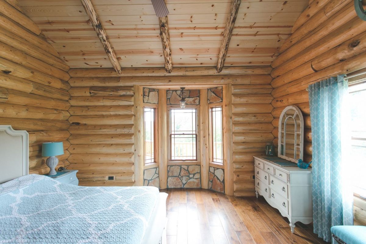 bay window behind blue bed in log cabin