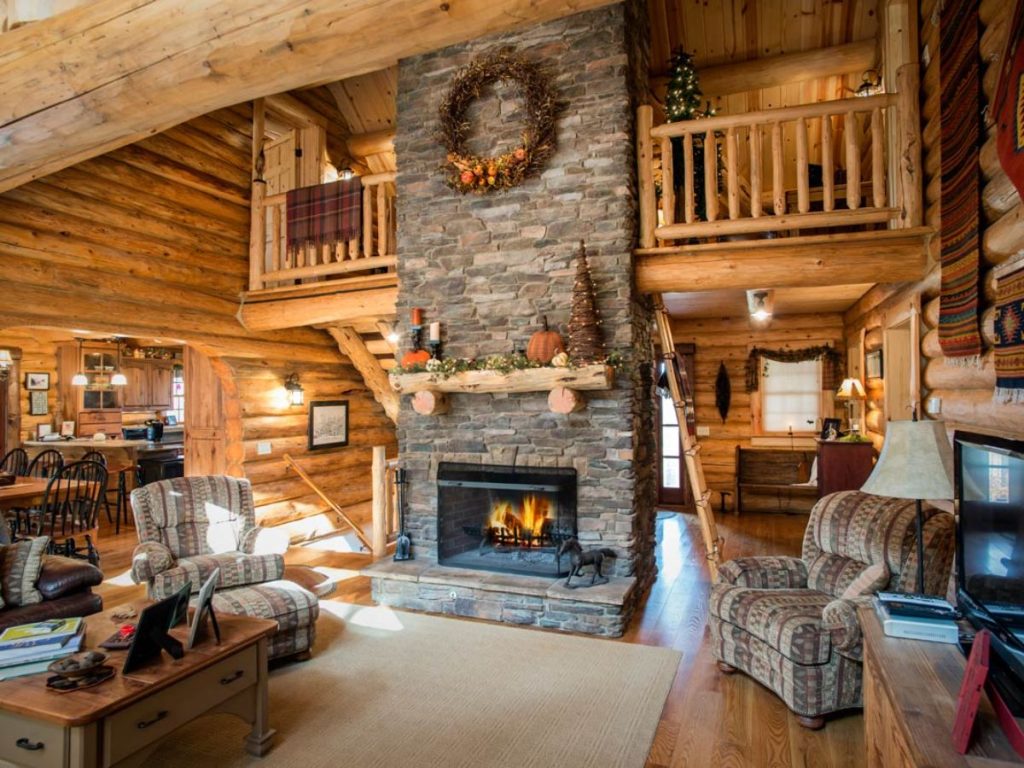 stone fireplace in center of room with loft behind and sofa in front