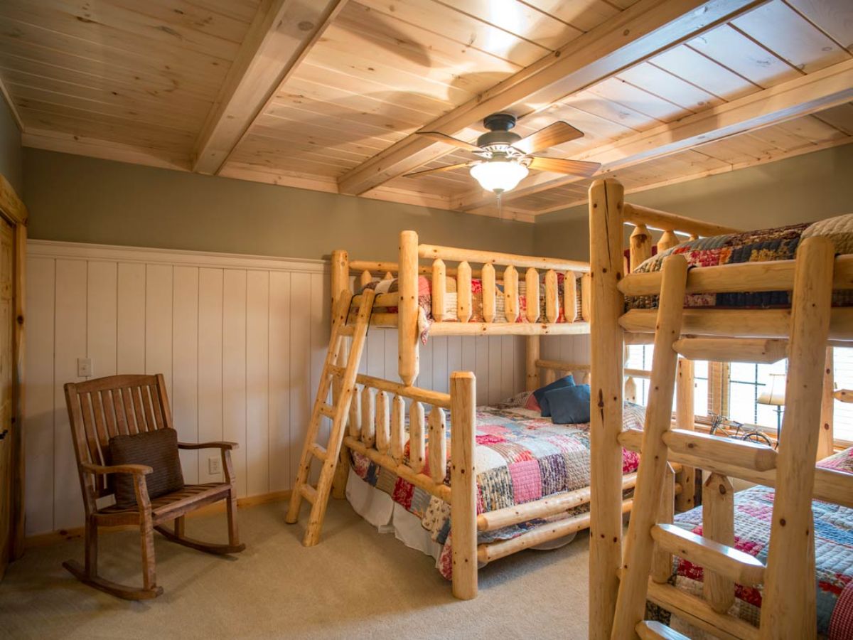 wood bunk beds underneath ceiling with fan next to rocking chair in cabin