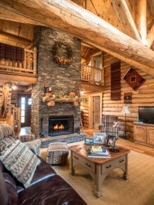 stone fireplace on far wall with brown leather sofa on left side of log cabin living space