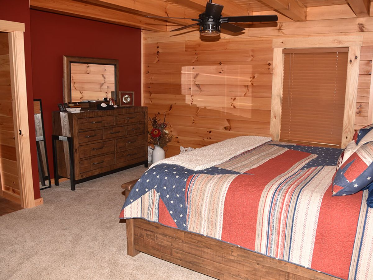 striped bedding on wood bedframe in log cabin bedroom with red wall on left and wood walls on other sides