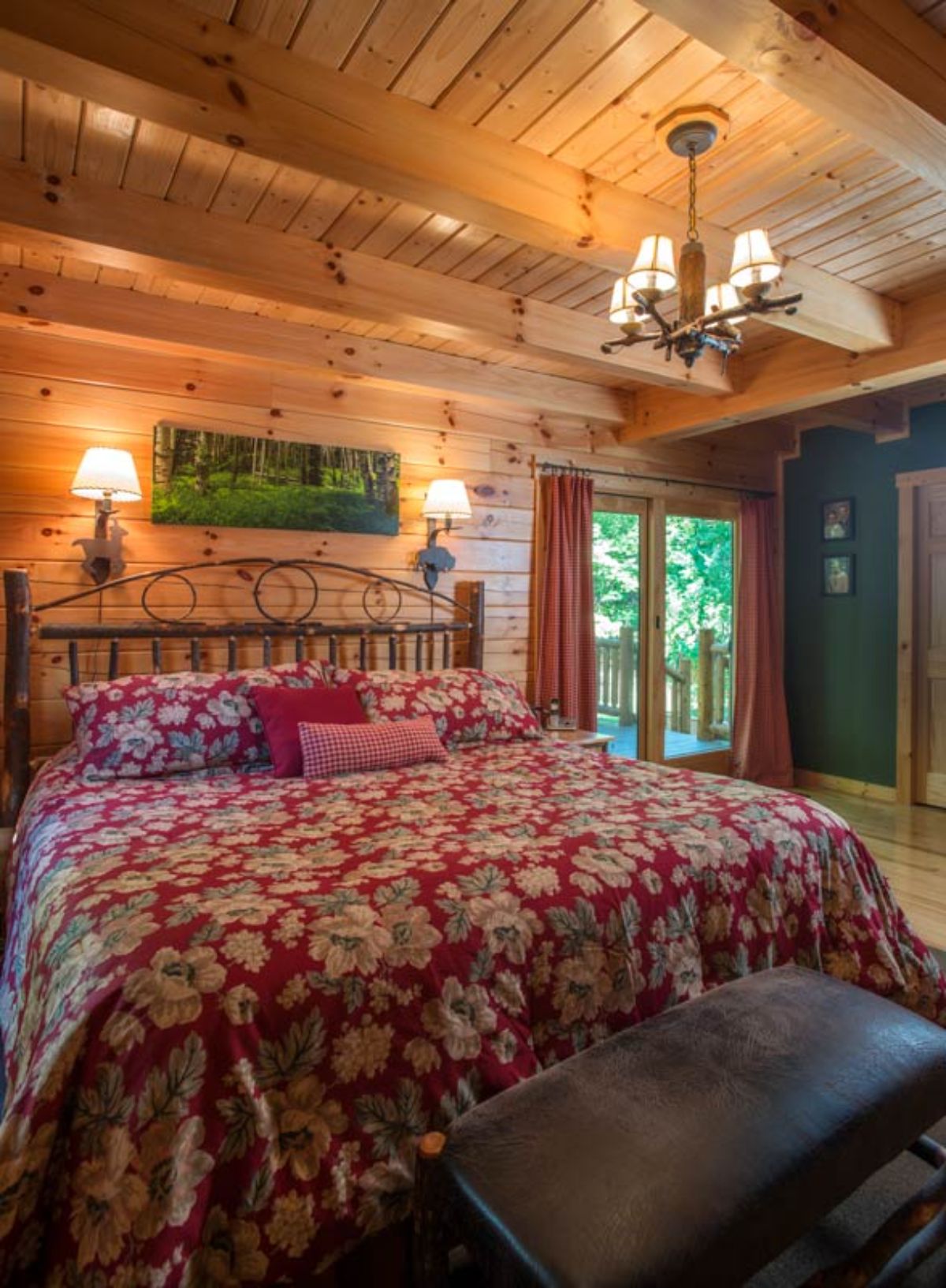 red floral bedding on wrought iron framed bed in log cabin with green sign above bed