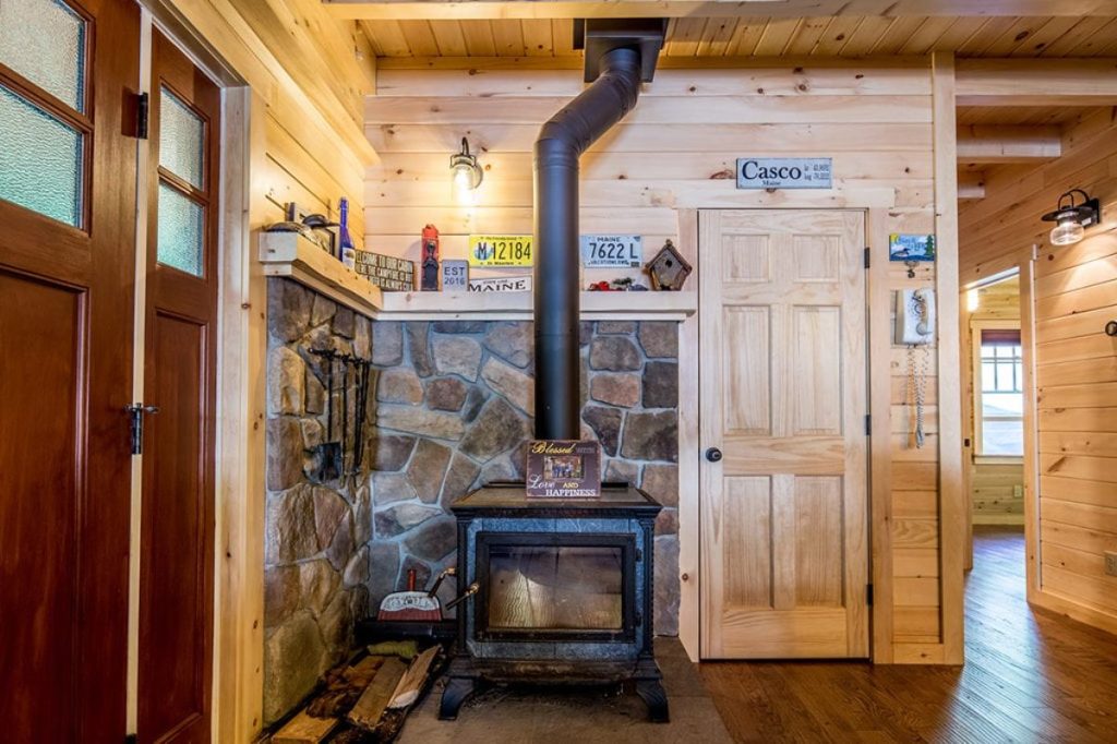 wood stove in corner with wood walls and stone wall behind stove
