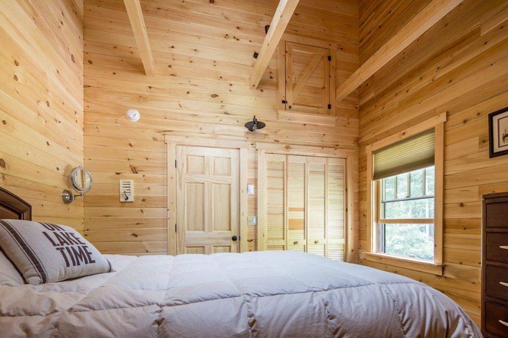 light gray bedding on bed in wood lined room