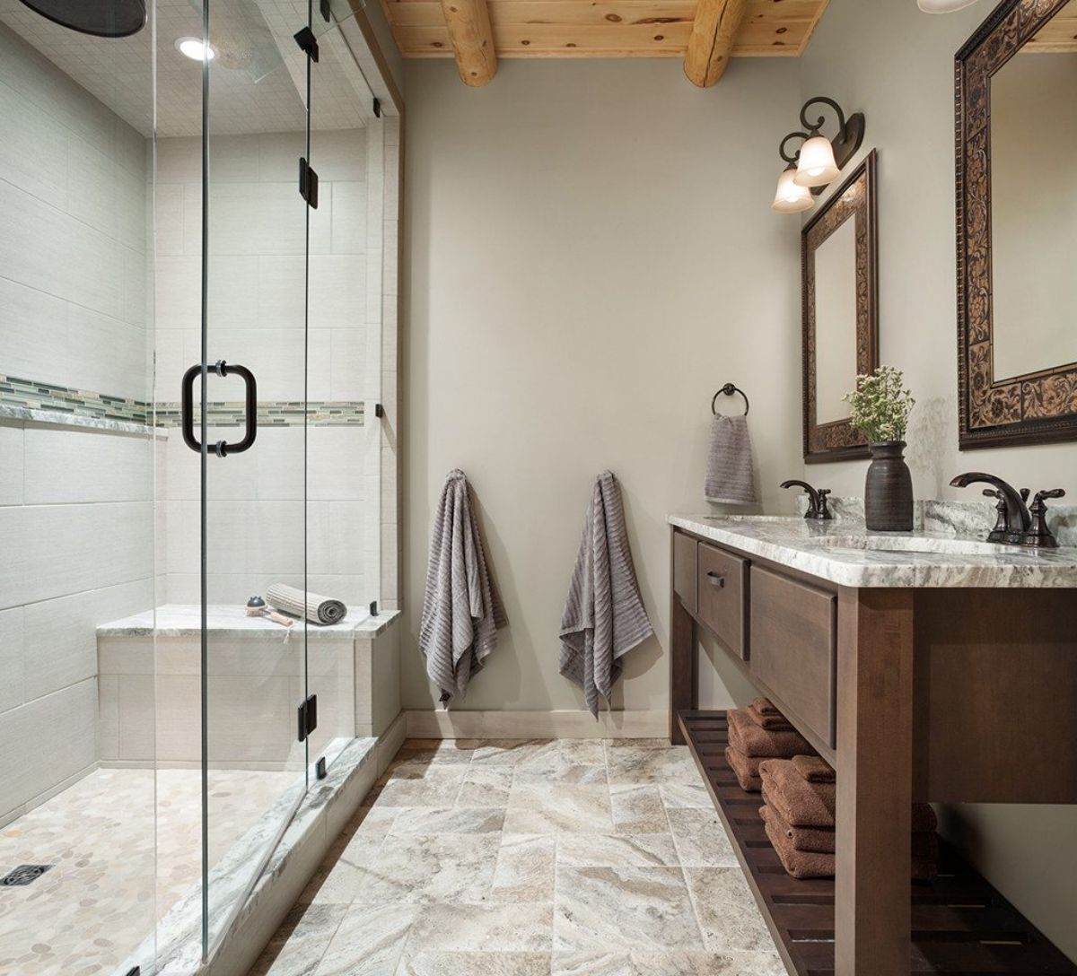 glass shower on left of bathroom with dark wood vanity beneath mirrors