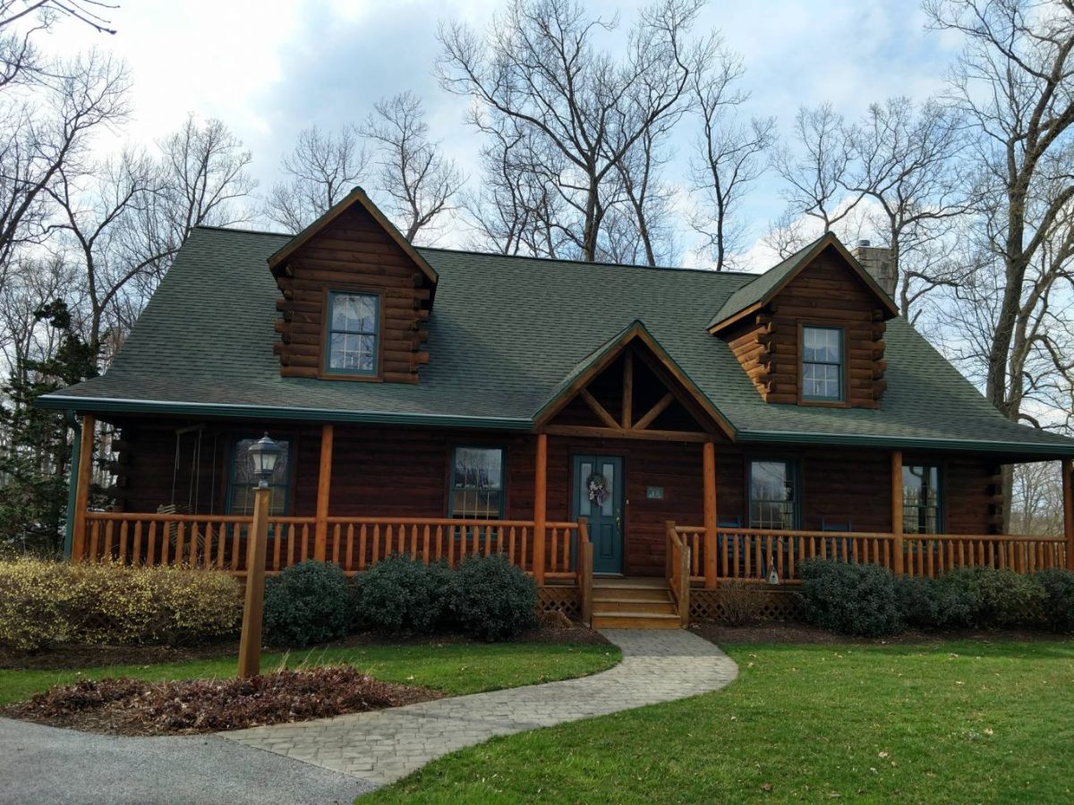 front porch on log cabin with dark wood trim and two dormer windows