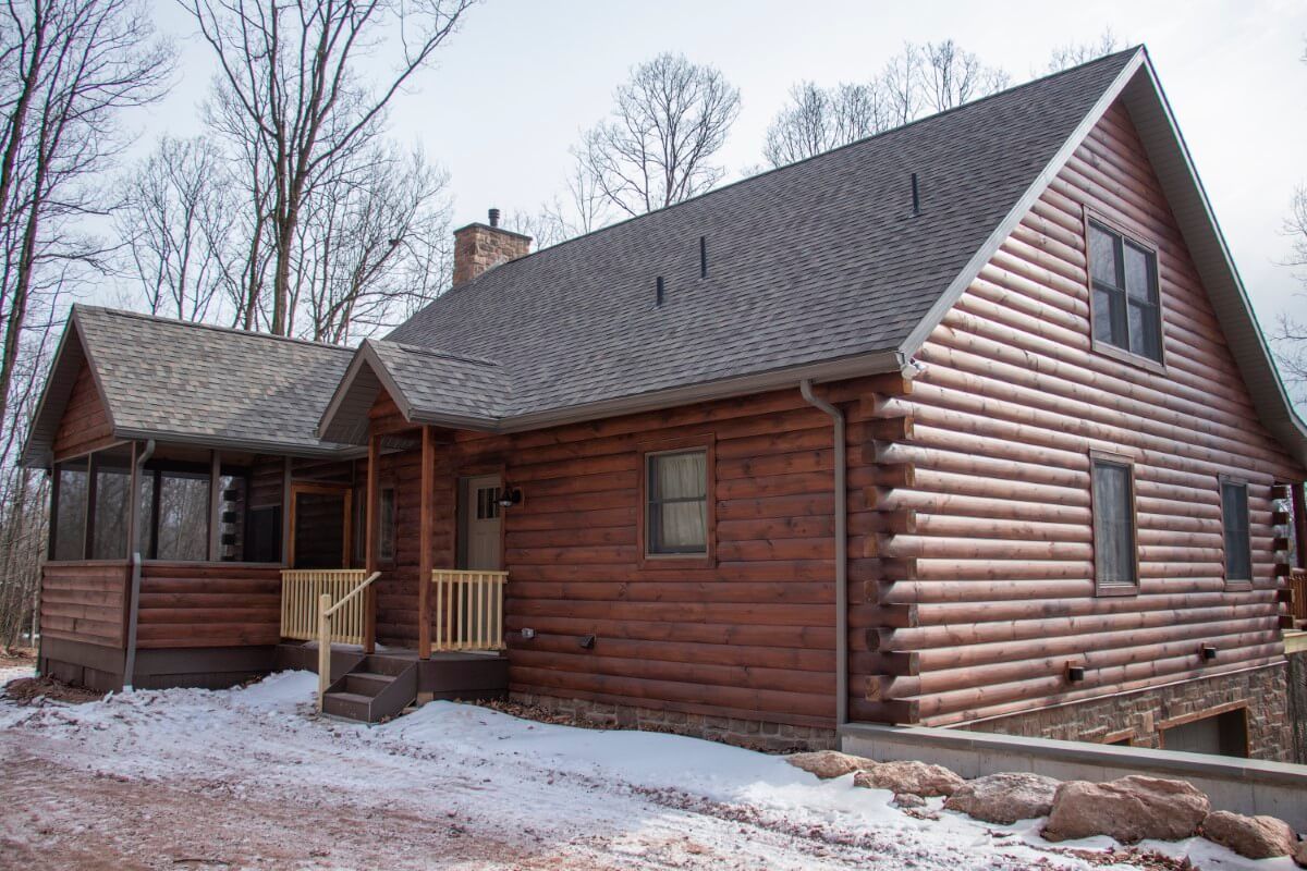 side of log cabin with gravel drive and small covered porch by back door