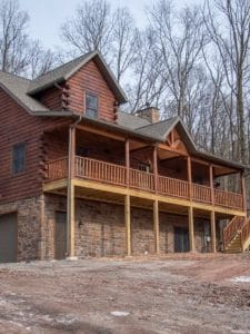 back of log cabin with stone bottom floor and dark wood lo siding with covered porch