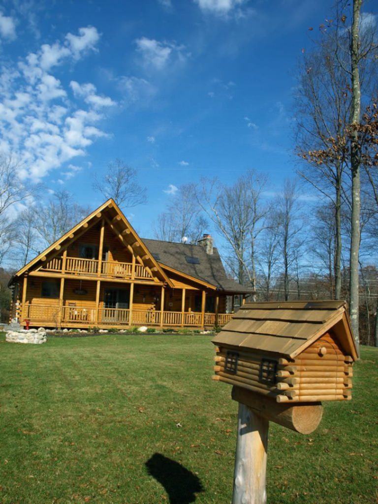 view of log cabin from drive with log mailbox in foreground