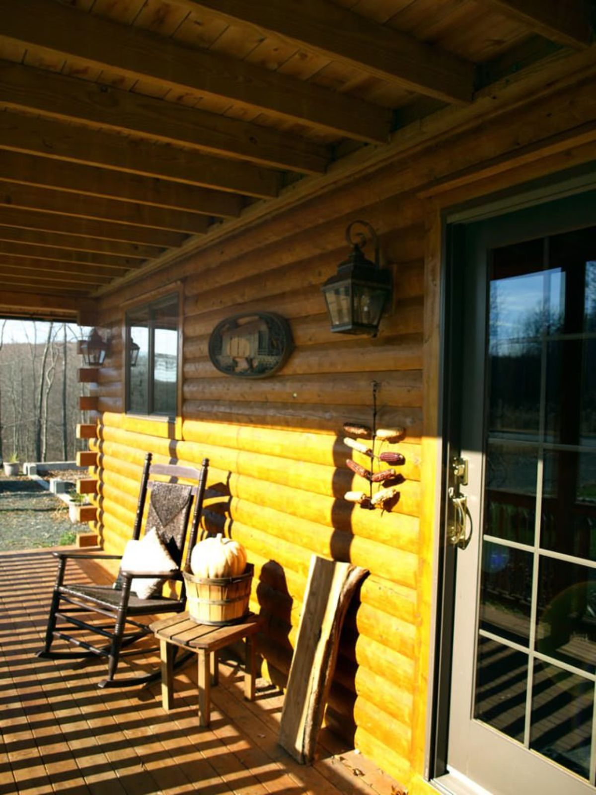 crocking chair against log wall on porch with glass paned door in foreground