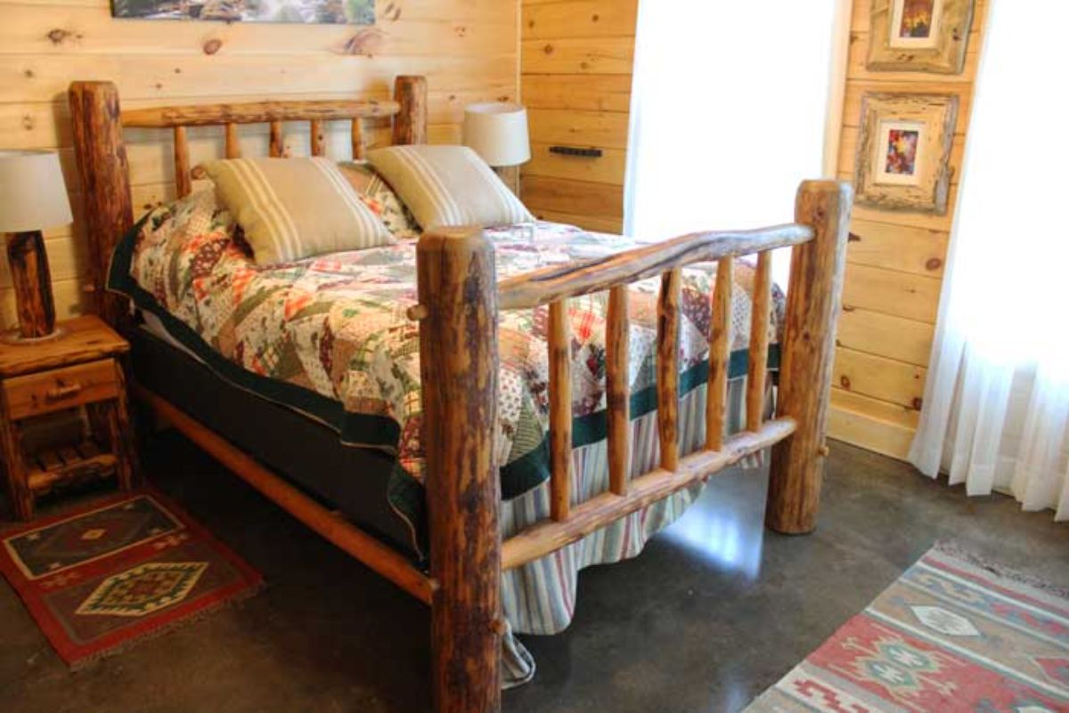 wood bedframe in bedroom with windows on side