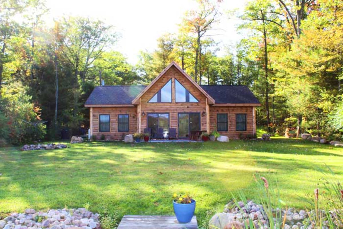 log cabin with wall of windows in center and open grass yard in foreground