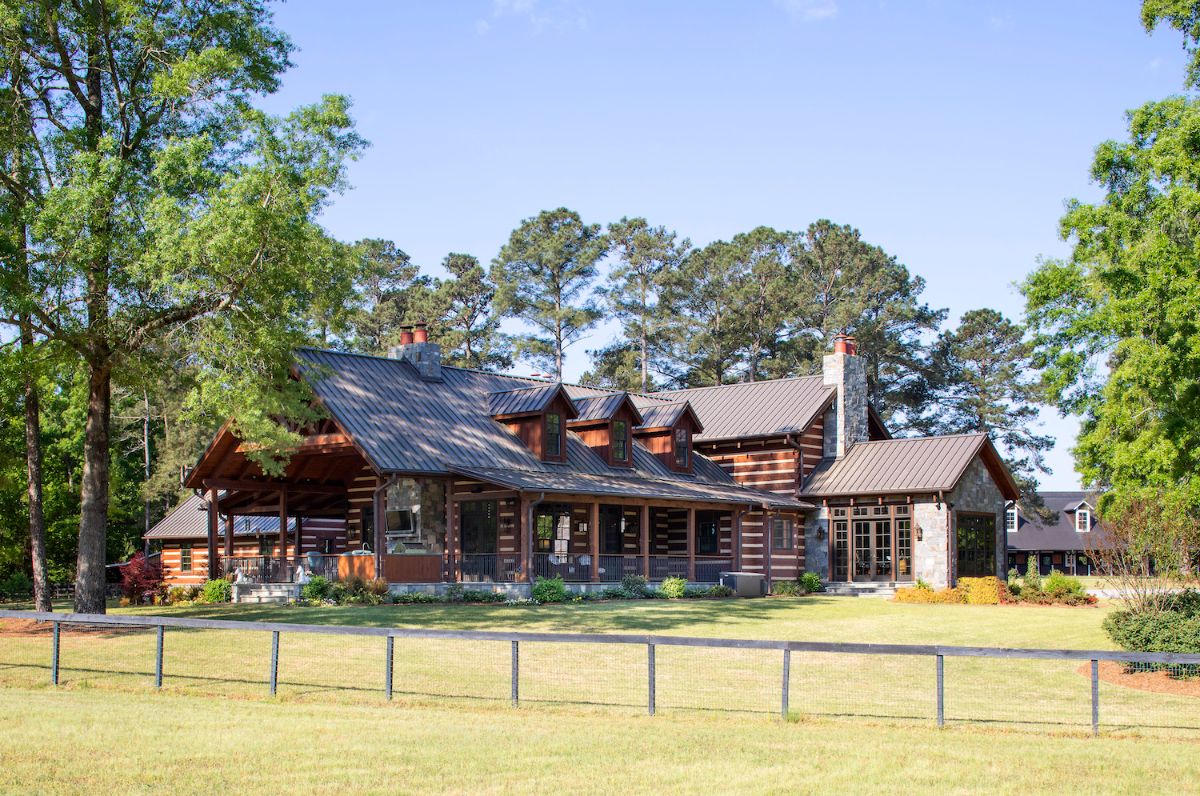 sprawling log cabin with covered front porch behind simple fenceline