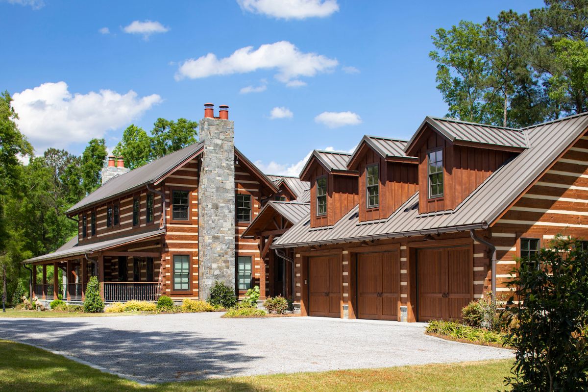 log cabin with two stories and chimney on end with 3 car attached garage