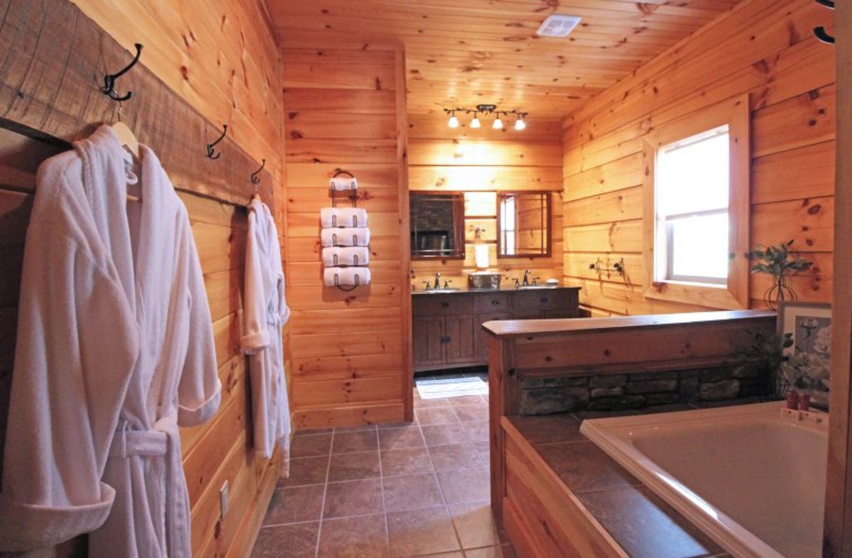 soaking tub in foreground with white robes on hooks on left