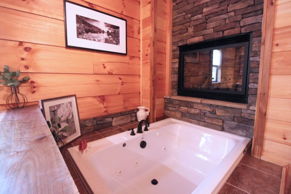 white soaking tub in stone surround with black trimmed mirror