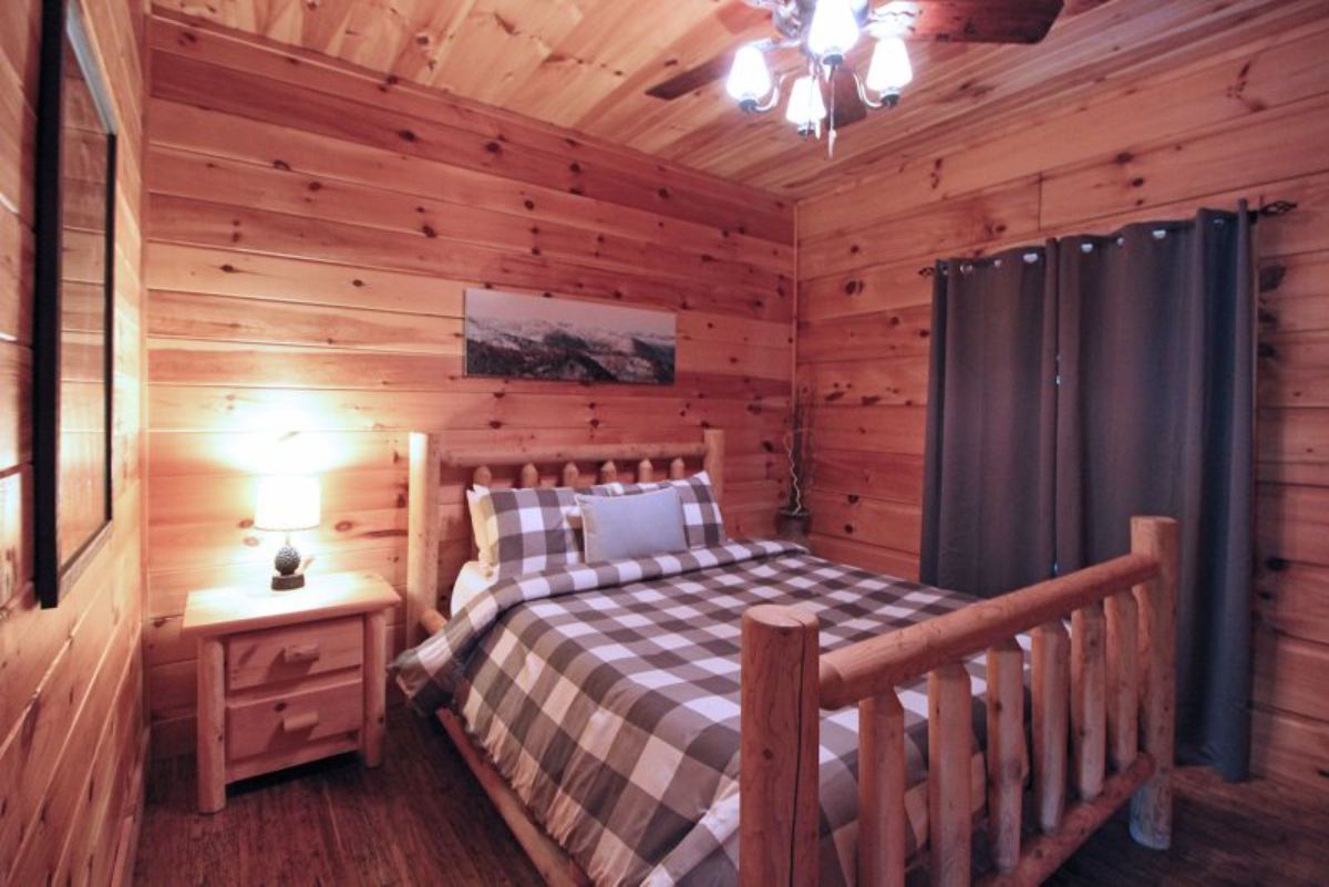 plaid bedding on small bed against log wall with green curtain