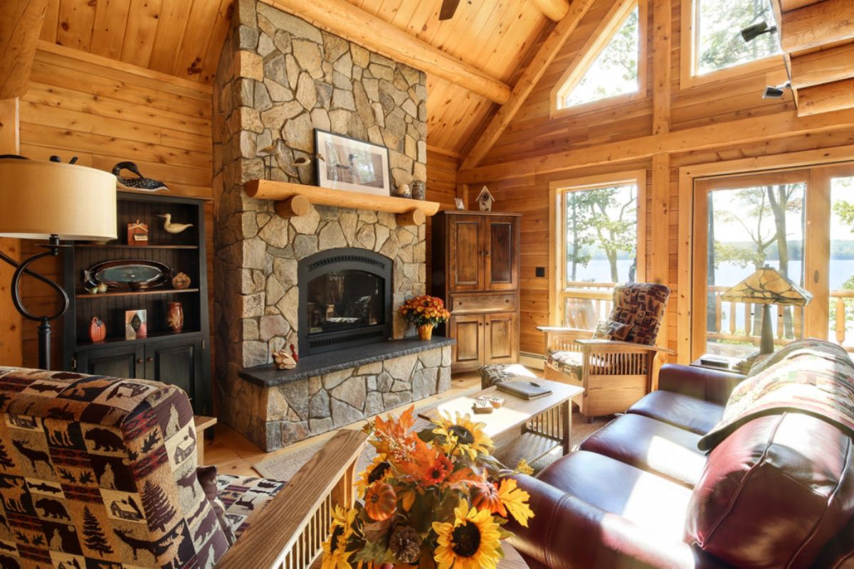 stone fireplace against log wall with windows on right and brown sofa in foreground