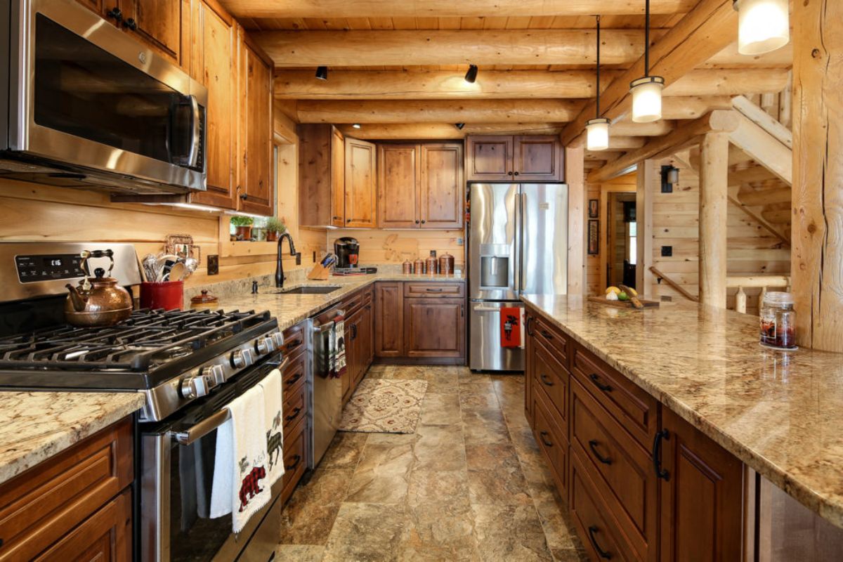 wood cabinets below granite countertop with stainless steel gas stove in foreground left
