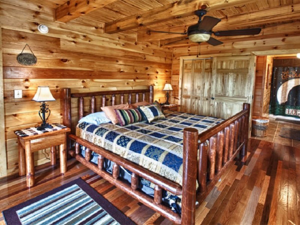 blue and white bedding on dark wood log frame bed in log cabin with sheer curtains on windows in background