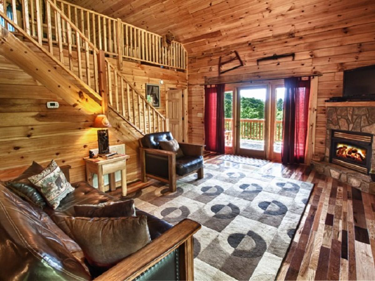 stairs to loft behind chairs in living room of log cabin
