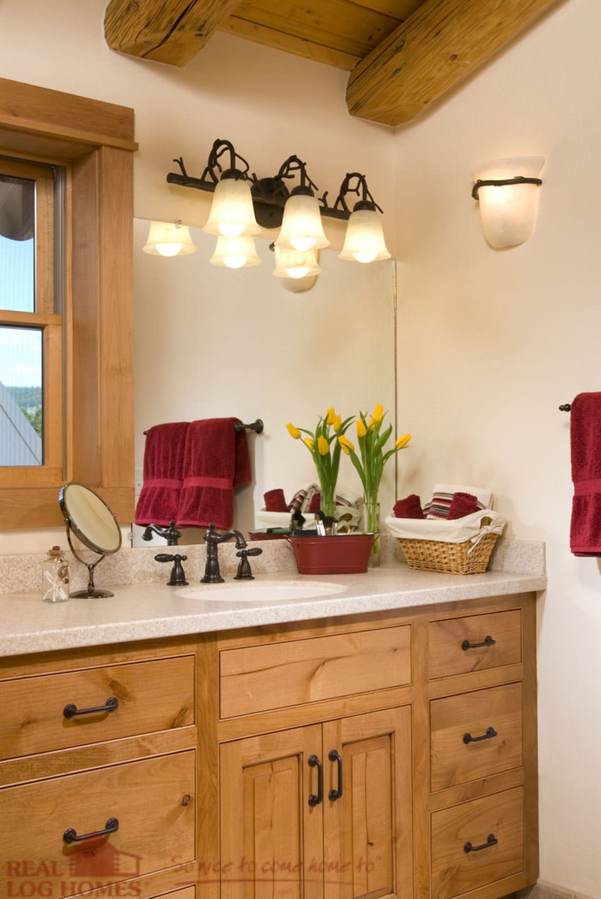 light wood cabinets under white counter tops in bathroom with maroon accent towels