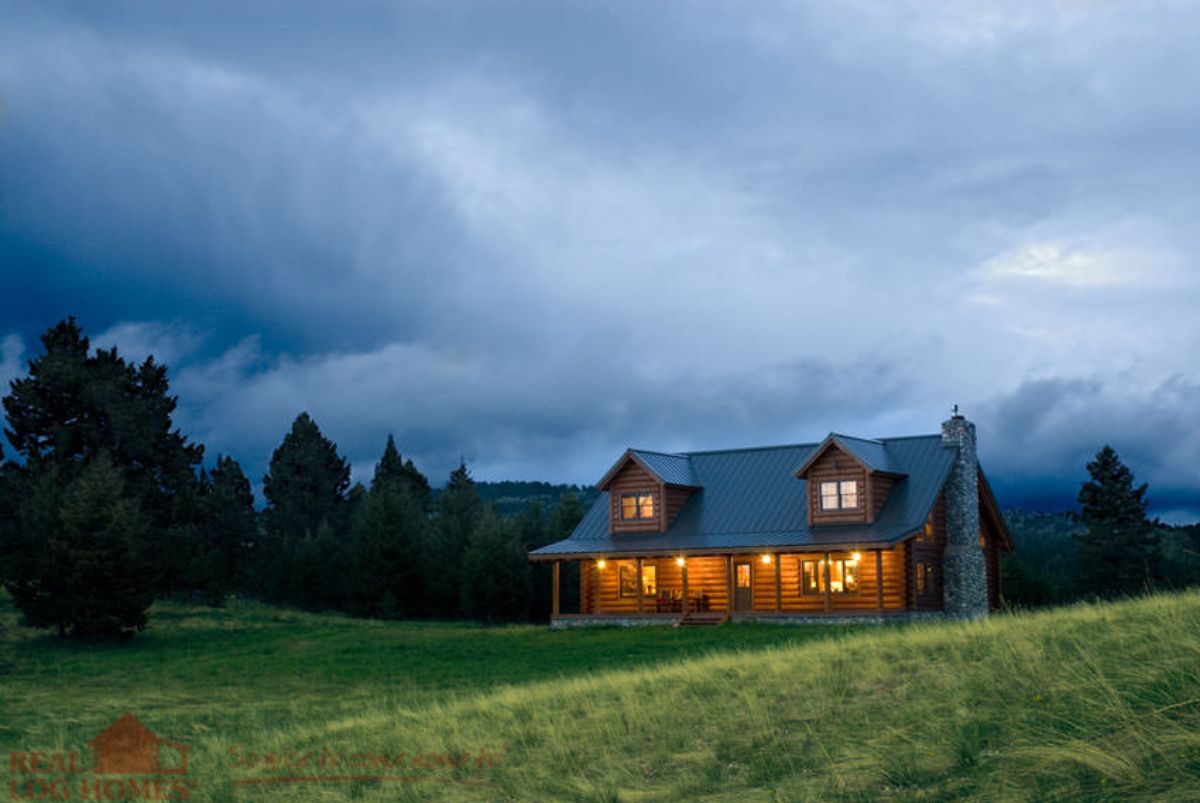 log cabin on hill with clouds above and trees in background