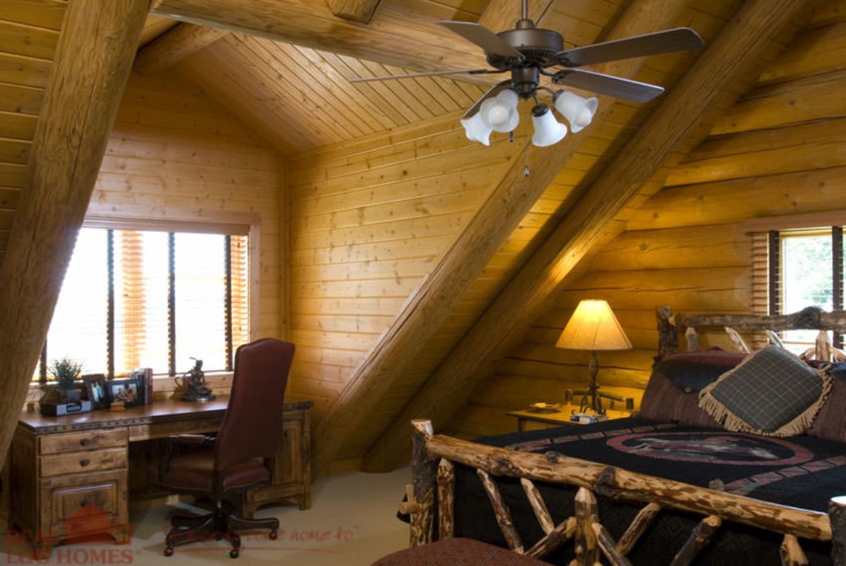 log frame bed with dark bedding in loft bedroom with desk and chair at dormer window